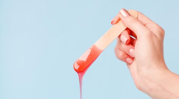 A wooden flat waxing stick, dripping hot depilatory wax.